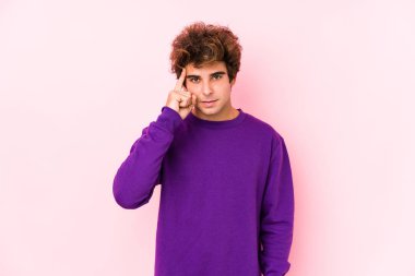 Pembe arka planda genç beyaz bir adam. Bir tapınağı işaret ediyor, düşünüyor ve bir göreve odaklanıyor..