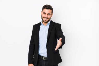 Beyaz arka planda beyaz tenli genç beyaz bir iş adamı kameraya doğru elini uzatarak selam veriyor..