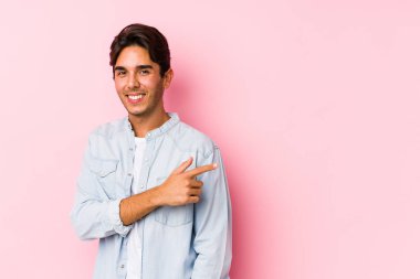 Pembe arka planda poz veren beyaz bir genç yalnız başına gülümseyip, boş alanda bir şeyler gösteriyor..