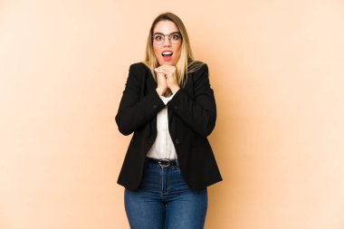 Middle age business woman isolated on beige background praying for luck, amazed and opening mouth looking to front.