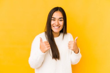 Sarı arka planda izole edilmiş genç bir kadın. Baş parmağını kaldırıyor, gülümsüyor ve kendinden emin..