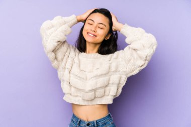 Mor arka planda izole edilmiş genç Çinli kadın ellerini başının üstünde tutarak neşe içinde gülüyor. Mutluluk kavramı.