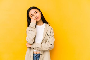 Sarı arka planda izole edilmiş genç Çinli bir kadın üzgün ve düşünceli bir şekilde fotokopi odasına bakıyor..