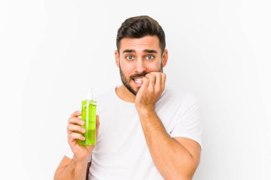 Genç, beyaz bir adam elinde aloe vera ile nemlendirici tutuyor. Tırnaklarını yiyor. Gergin ve endişeli..
