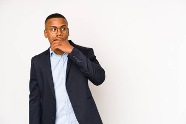 Young business latin man isolated on white background thoughtful looking to a copy space covering mouth with hand.