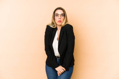 Middle age business woman isolated on beige background shrugs shoulders and open eyes confused.