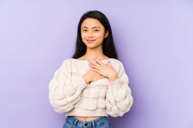 Mor bir arka planda izole edilmiş genç Çinli kadın, avuçlarını göğsüne bastıran dostça bir ifadeye sahiptir. Aşk konsepti.