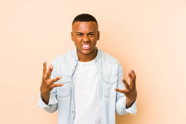 Young latin man isolated on beige background upset screaming with tense hands.