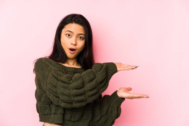 Pembe arka planda izole edilmiş genç Çinli kadın elleri arasında bir kopya alanı tutarken şok olmuş ve hayrete düşmüş..