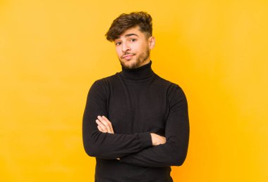 Sarı arka planda izole edilmiş genç Arap adam alaycı bir ifadeyle kameraya bakıyor..