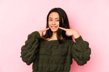 Pembe bir arka planda izole edilmiş genç Çinli kadın gülümsüyor, parmaklarını ağıza doğrultuyor..