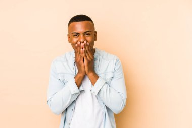 Young latin man isolated on beige background laughing about something, covering mouth with hands.
