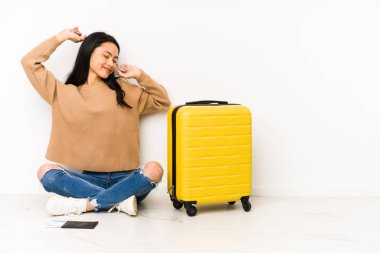 Genç Çinli gezgin kadın elinde bavulla yerde oturmuş özel bir günü kutluyor, atlıyor ve enerji dolu kollarını kaldırıyor..