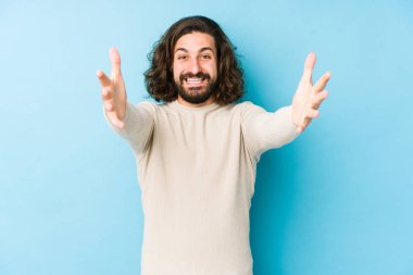 Mavi arka planda izole edilmiş genç, uzun saçlı adam kameraya sarıldığı için kendinden emin hissediyor..