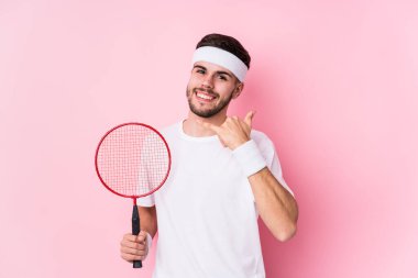 Badminton oynayan beyaz bir adam izole edilmiş, parmaklarıyla bir cep telefonu hareketi gösteriyor..