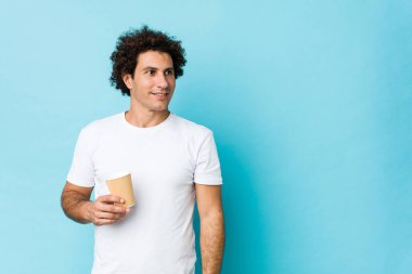 Kafkasyalı kıvırcık adam elinde kahve ile kollarını kavuşturup gülümsüyor..