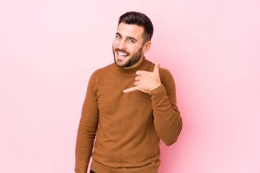 Pembe arka planda genç beyaz bir adam izole edilmiş, parmakları olan bir cep telefonu hareketi gösteriyor..