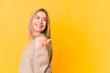 Sarışın, beyaz bir kadın. Sarı arka planda izole edilmiş. Baş parmak uzakta, gülüyor ve kaygısız..