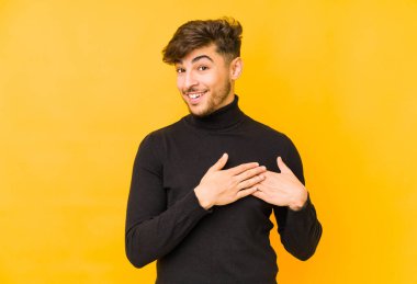Sarı arka planda izole edilmiş genç bir Arap adam, avuçlarını göğsüne bastıran dostane bir ifadeye sahiptir. Aşk konsepti.