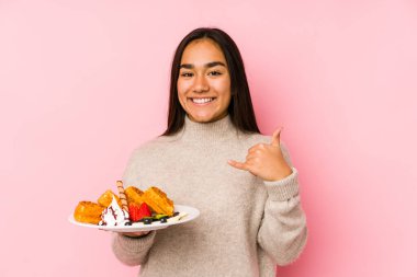 Genç Asyalı kadın bir waffle tutuyor. İzole edilmiş. Cep telefonu hareketini parmaklarıyla gösteriyor..