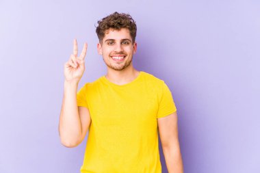 Sarışın, kıvırcık saçlı, beyaz tenli bir adam iki numarayı parmaklarıyla gösteriyor..