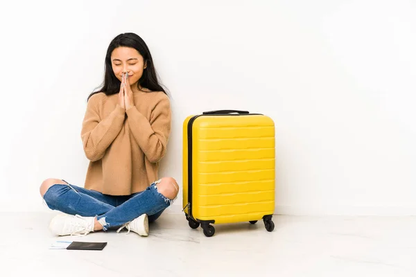 若い中国人旅行者の女性が座っている床の上にスーツケースで隔離された手を口の近くで祈る 自信を感じる — ストック写真