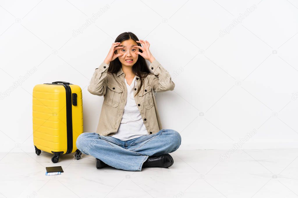 Young chinese traveler woman sitting holding a boarding passes keeping eyes opened to find a success opportunity.