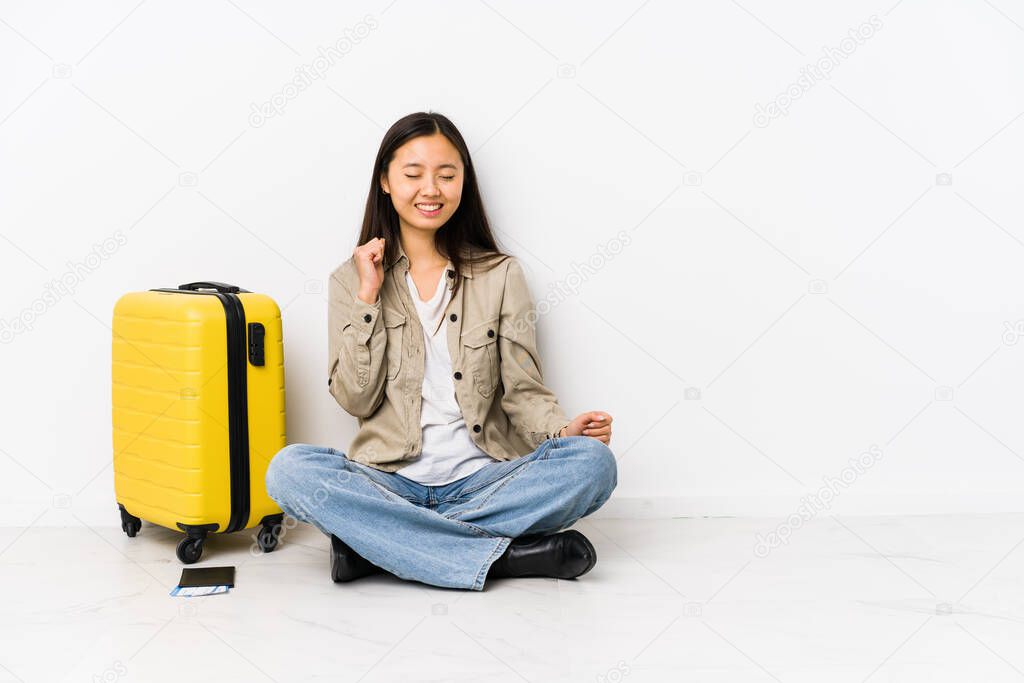 Young chinese traveler woman sitting holding a boarding passes dancing and having fun.