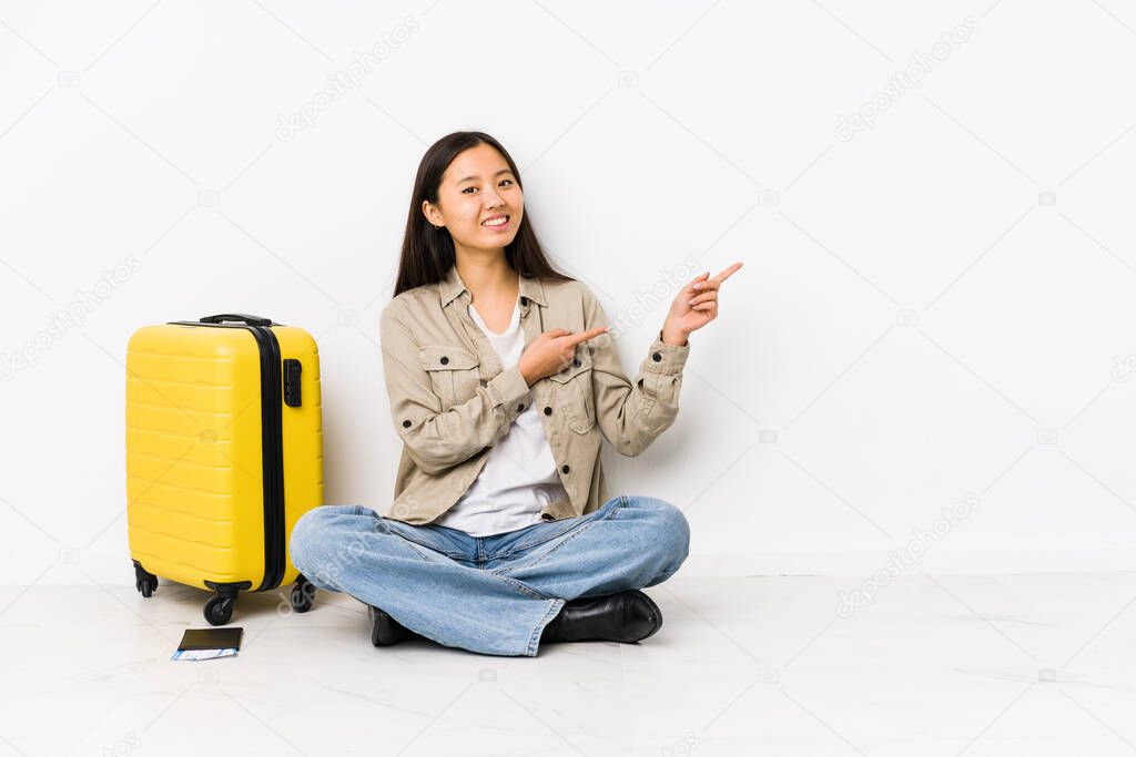 Young chinese traveler woman sitting holding a boarding passes excited pointing with forefingers away.