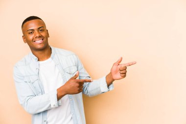 Young latin man isolated on beige background excited pointing with forefingers away. clipart