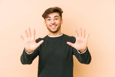 Genç Arap adam bej bir arka planda izole edilmiş. Elleriyle on numarayı gösteriyor..