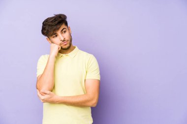 Mor bir arka planda izole edilmiş, üzgün ve dalgın hisseden genç bir Arap kopyalama alanına bakıyor..