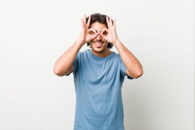 Beyaz arka planda genç ve yakışıklı bir adam. Gözlerinde işaret var.