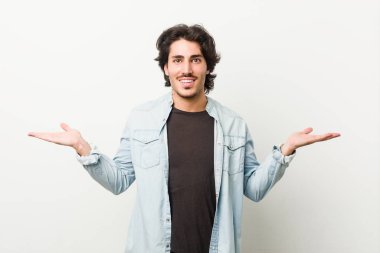 Beyaz bir geçmişi olan genç yakışıklı bir adam kollarıyla ölçeği yapıyor, mutlu ve kendinden emin hissediyor..