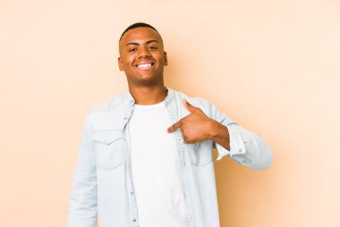 Latin kökenli genç bir adam bej arka planda izole edilmiş. Elle bir gömlek fotokopisini gösteriyor. Gururlu ve kendinden emin.