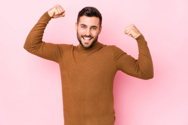 Pembe arka planda genç beyaz bir adam izole edilmiş kollarıyla güçlü bir hareket gösteriyor, kadınsı gücün sembolü.