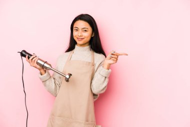 Genç Çinli bir kadın mikser tutuyor. Kafasının arkasına dokunuyor, düşünüyor ve bir seçim yapıyor..