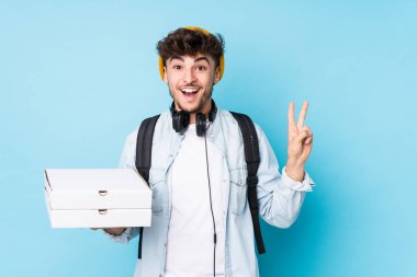 Elinde pizza tutan genç Arap öğrenci neşeli ve tasasız parmaklarıyla barış sembolü gösteriyor..