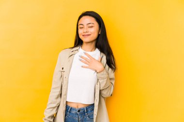 Sarı arka planda izole edilmiş genç Çinli kadın elini göğsünde tutarak kahkahalar atıyor..