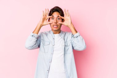 Pembe arka planda poz veren beyaz genç bir adam, izole edilmiş bir şekilde, bir başarı fırsatı bulmak için gözlerini açık tutuyor..