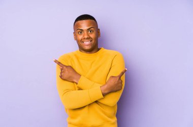 Mor arka plan noktalarında izole edilmiş genç latin adam iki seçenek arasında seçim yapmaya çalışıyor..