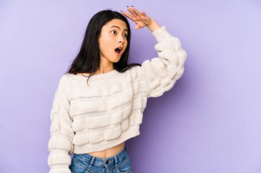 Mor bir arka planda izole edilmiş genç Çinli kadın uzaklara bakıyor ve elini alnına koyuyor..