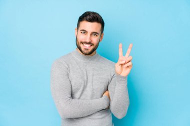 Mavi arka planda genç beyaz bir adam iki numarayı parmaklarıyla gösteriyor..