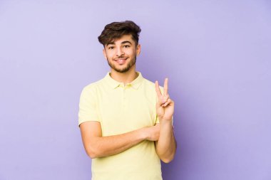 Mor arka planda izole edilmiş genç bir Arap adam iki numarayı parmaklarıyla gösteriyor..