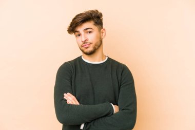 Genç Arap bir adam bej bir arka planda izole edilmiş. Kameraya alaycı bir ifadeyle bakıyor..