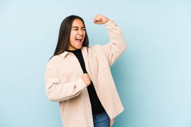 Mavi arka planda izole edilmiş genç bir kadın zafer sonrası yumruğunu kaldırıyor, kazanan konsept..