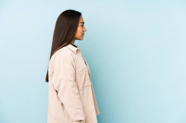 Genç bir kadın mavi arka planda izole edilmiş, sola bakıyor, yandan poz veriyor..