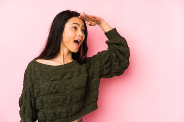 Pembe arka planda izole edilmiş genç Çinli kadın uzaklara bakıyor ve elini alnına koyuyor..