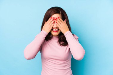 Orta yaşlı, soyutlanmış bir Latin kadın elleriyle gözlerini kapatıyor, gülümseyerek bir sürpriz bekliyor..