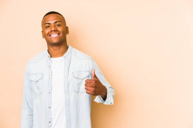 Young latin man isolated on beige background smiling and raising thumb up